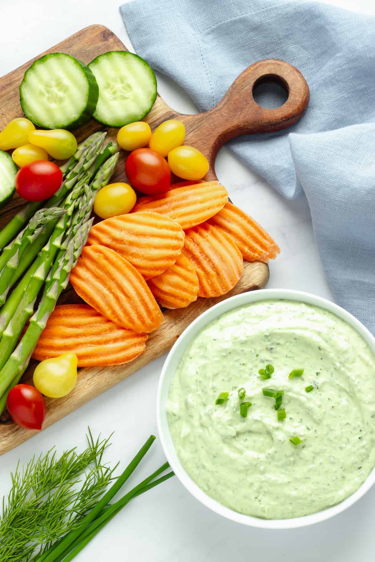 Image of a ramekin with green goddess dip and a cutting board with cut veggies for dipping.