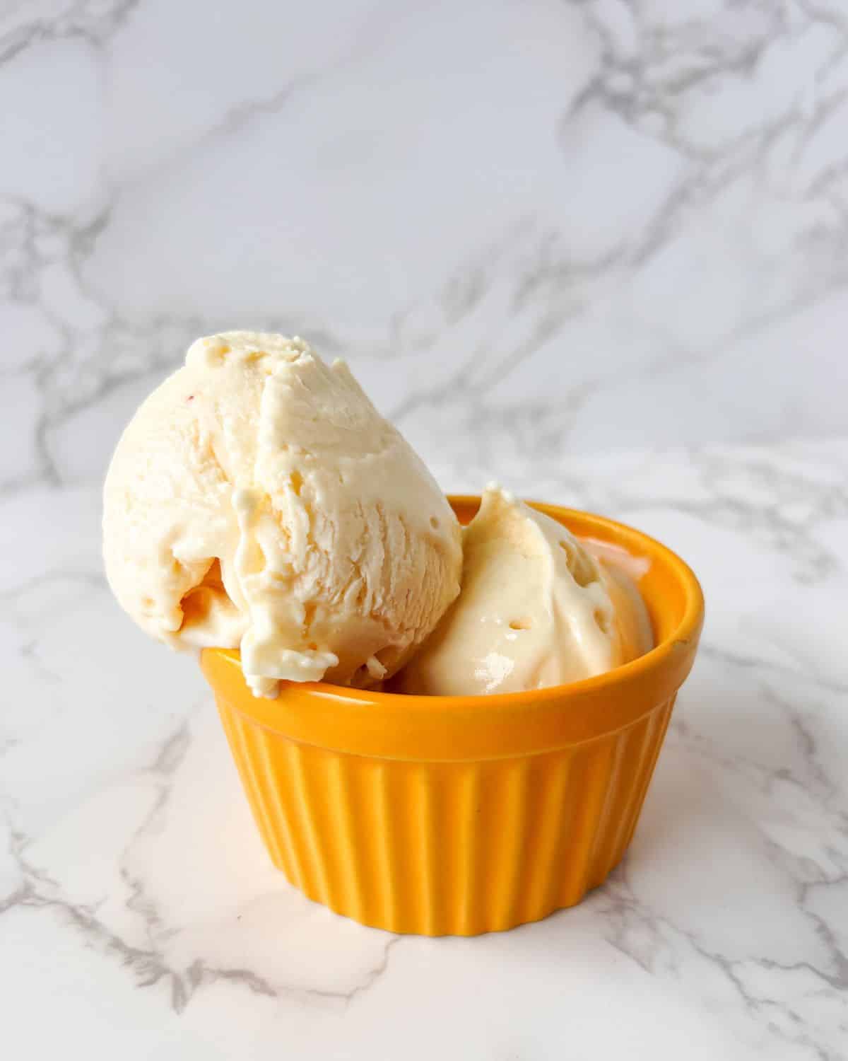 Image of a peach ramekin filled with 2 scoops of peach ice cream