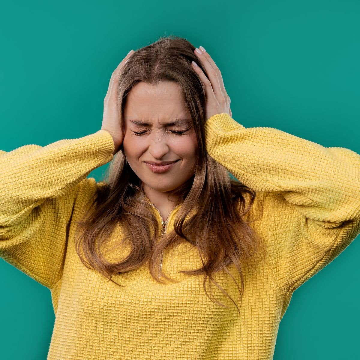 Image with green background and woman in yellow sweater holding her head